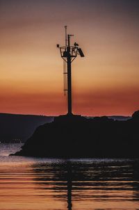 Silhouette telephone pole by sea against sky during sunset
