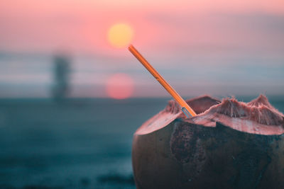 Close-up of coconut with straw against sky during sunset