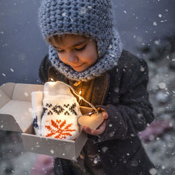 Pretty girl in knitted grey hat opening a crafted gift box with a new pair of gloves, snowfall