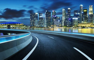 Illuminated road by buildings against sky at night