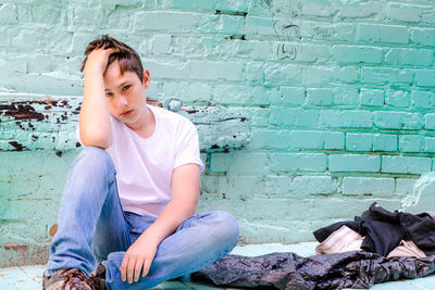 Full length of teenage boy sitting against wall