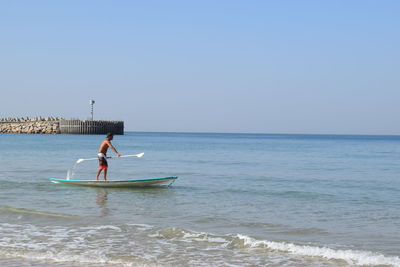 Man paddleboarding on sea against sky