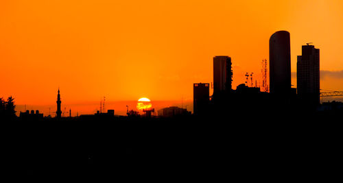 Silhouette buildings against orange sky during sunset