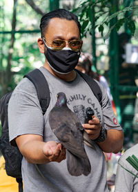 A man wearing sunglasses holding a pigeon on his hand.