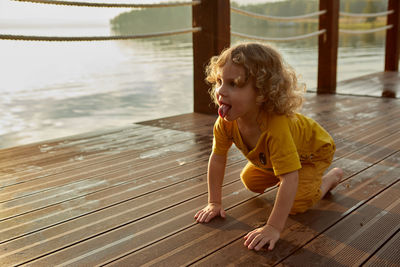 Girl looking away while crawling on wooden pier