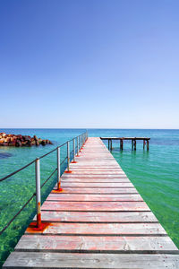 Pier over sea against clear blue sky