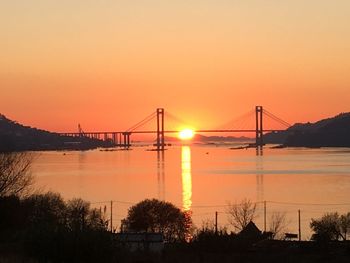 Silhouette bridge over river against orange sky