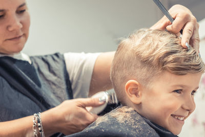 Close-up of female hairdresser styling boy hair in salon