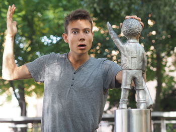 Portrait of shock young man standing by statue