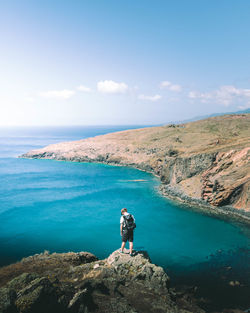 Man standing on rock by sea against sky