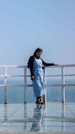 Portrait of smiling woman standing by railing against sky