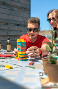 Concentrated man catching jenga game piece next to colleague on terrace