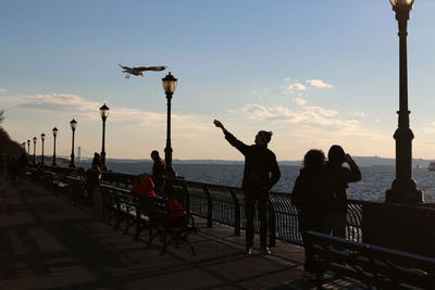 People on pier by hudson river against sky during sunny day