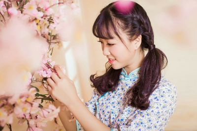Young woman with pink flowers against tree