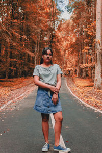 Portrait of young woman standing on road against trees