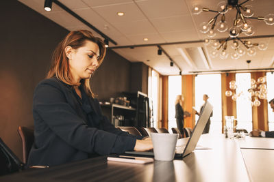 Serious female financial advisor working on laptop at conference table in board room