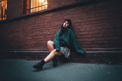 Portrait of young woman sitting against brick wall