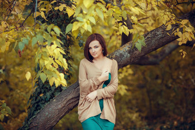 Young woman standing by tree