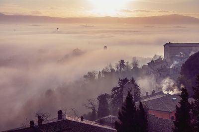 High angle view of buildings against cloudy sky during foggy weather at sunset