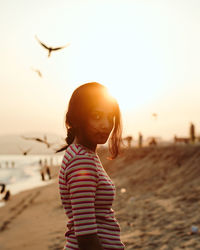Girl standing on beach against sky during sunset