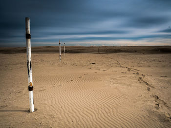 Wooden posts on sand at beach against sky