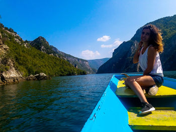 Woman sitting in boat against blue sky