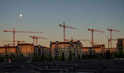 Cranes in city against clear sky during sunset