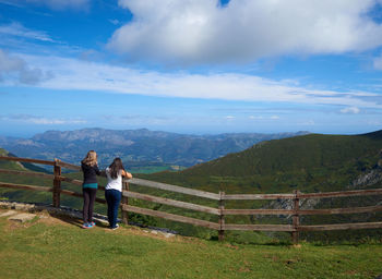 Rear view of women standing by railing against mountains and sky