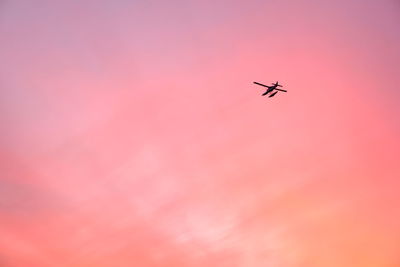 Low angle view of silhouette airplane flying against dramatic sky during sunset