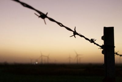 Silhouette of barbed wire fence on field during sunset