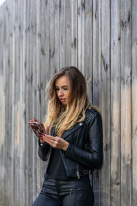 Young woman with blond hair using phone by wooden fence