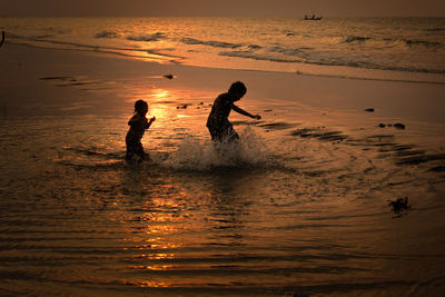 Silhouette people on beach against sky during sunset