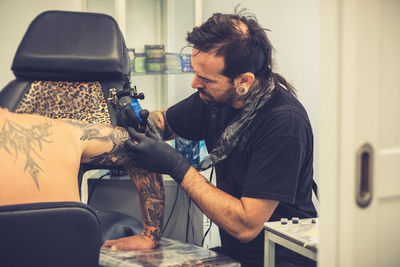 Artist making tattoo on shirtless man shoulder