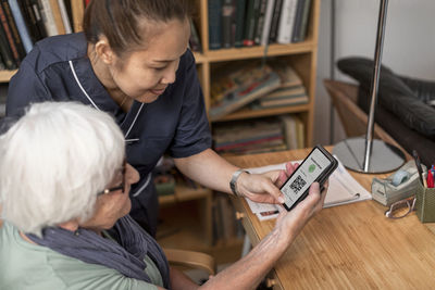 Home carer helping senior woman to use cell phone with covid-19 vaccine certificate