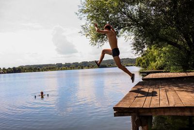 Full length of shirtless man jumping in lake against sky