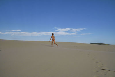 Woman walking on sandy beach against sky