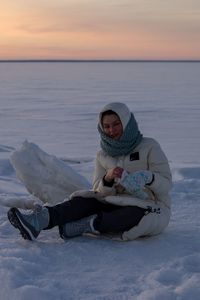 Portrait of woman sitting on snow during sunset