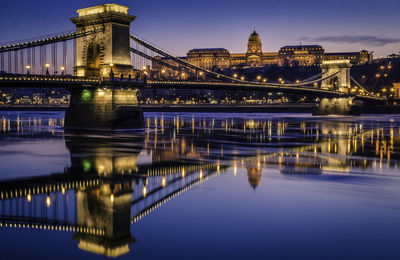 Illuminated bridge over river in city at night