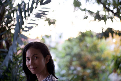 Portrait of smiling young woman against trees