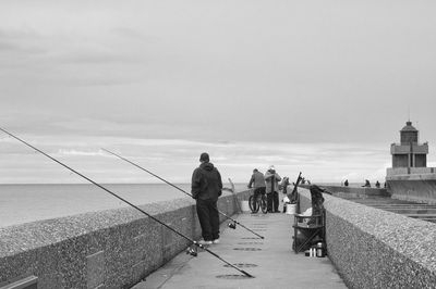 Rear view of people on railing by sea against sky