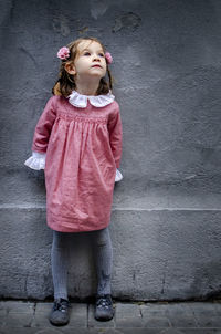 Girl looking away while standing against gray wall
