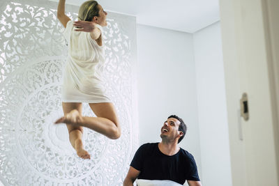 Full length of woman jumping indoors with man looking at her