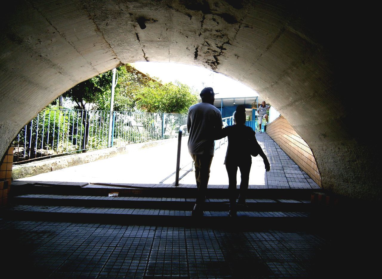 REAR VIEW OF MAN AND WOMAN WITH ARMS