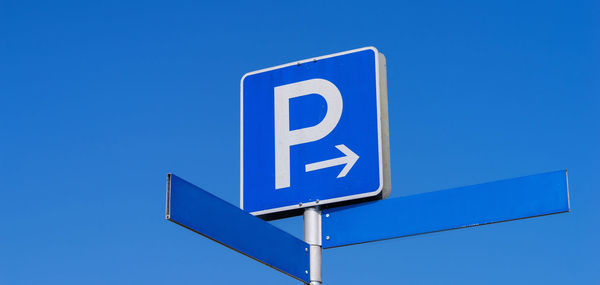 Low angle view of road sign against clear blue sky