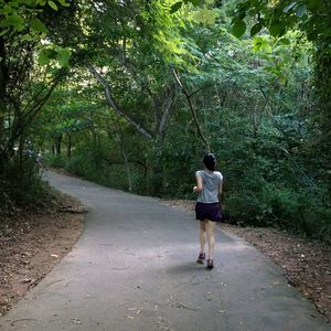 Rear view of young woman jogging on road in forest