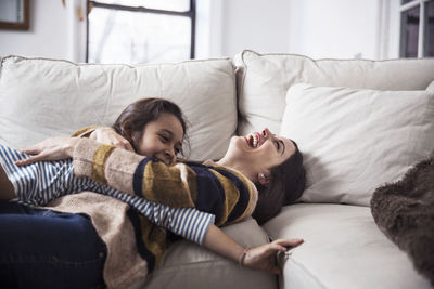 Cheerful mother and daughter enjoying on sofa at home