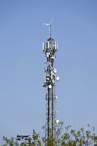 Low angle view of communications tower with wind turbine against clear sky