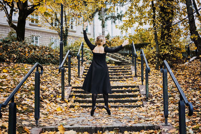 Ballerina dancing in autumn city street, modern ballet dancer in black dress, pointe shoes outdoors