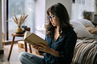 Woman reading book while sitting at home