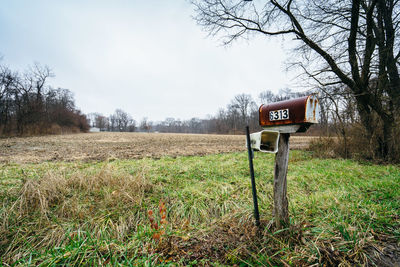 Information sign on field by trees against sky